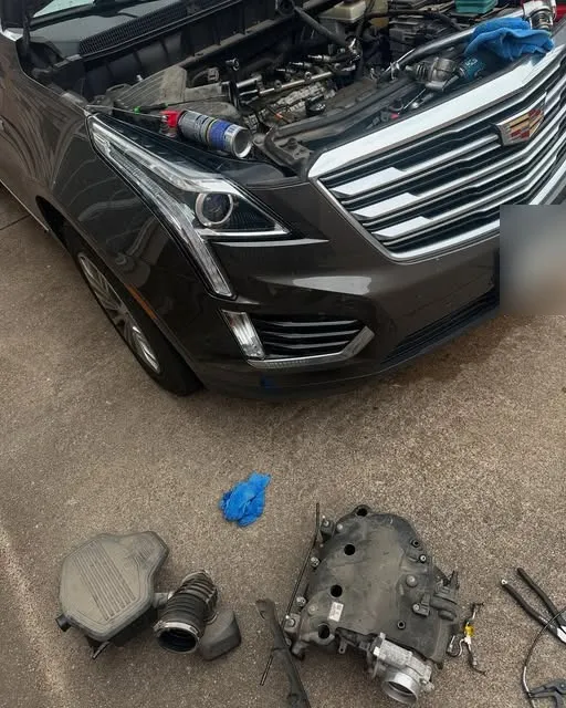 Cadillac SUV with the hood open and its intake manifold and air intake parts laid out on the concrete