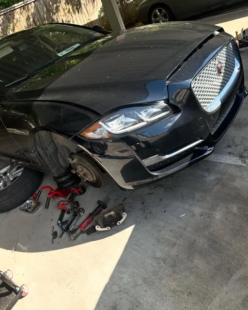 Black Jaguar sedan on a jack with the front wheel removed and tools on the ground