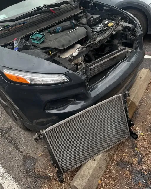 Car with the front end open and a radiator leaning against the bumper in a parking lot